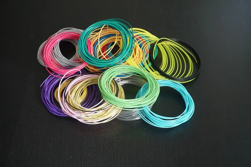 Loose coils of 1.75mm 3D printer filament in many colours on a dark surface