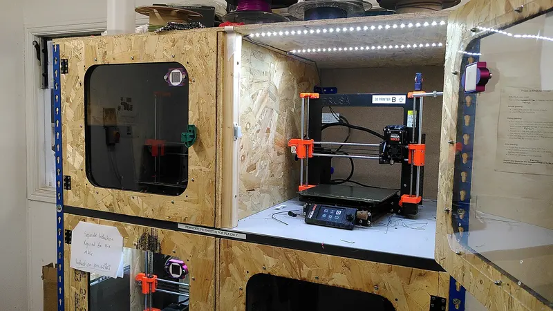 An FDM 3D printer inside a home-made enclosure built from OSB board with a clear window, at Bristol Hackspace